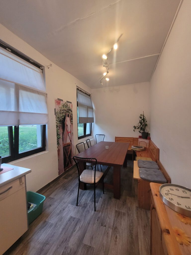 Der gemütliche Essbereich mit Holztisch, Stühlen, Sitzbänken, weißen Wänden und Fenstern mit Jalousien bietet eine perfekte Startseite für unvergessliche Mahlzeiten.